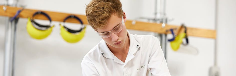 Male student wearing safety glasses and sanding a woodworking project