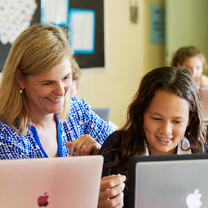 Female teacher and two female students laughing while looking at laptop screens