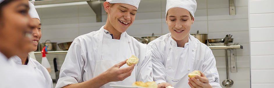 Vocational program students wearing chef uniforms and holding up scones