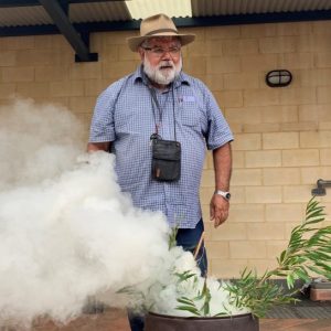 Dr. Noel Nannup behind smoking branches in a metal container.