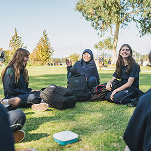 A group of students sitting on the grass in a circle, chatting and laughing.