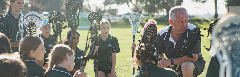 A teacher and students chatting together, all holding lacrosse equipment.