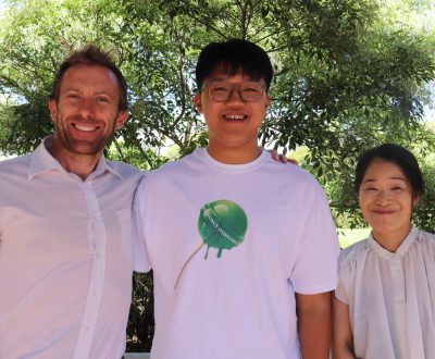 A smiling student (Inho Jung) standing between two proud-looking teachers, Mr Robbie Poole and Noriko Ikuta.